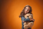 The cute cheerful little girl with Teddy bear on orange background